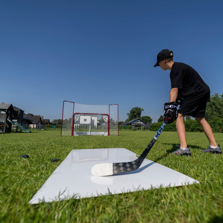 Young hockey player practicing wrist shots from a shooting pad toward a net in the garden