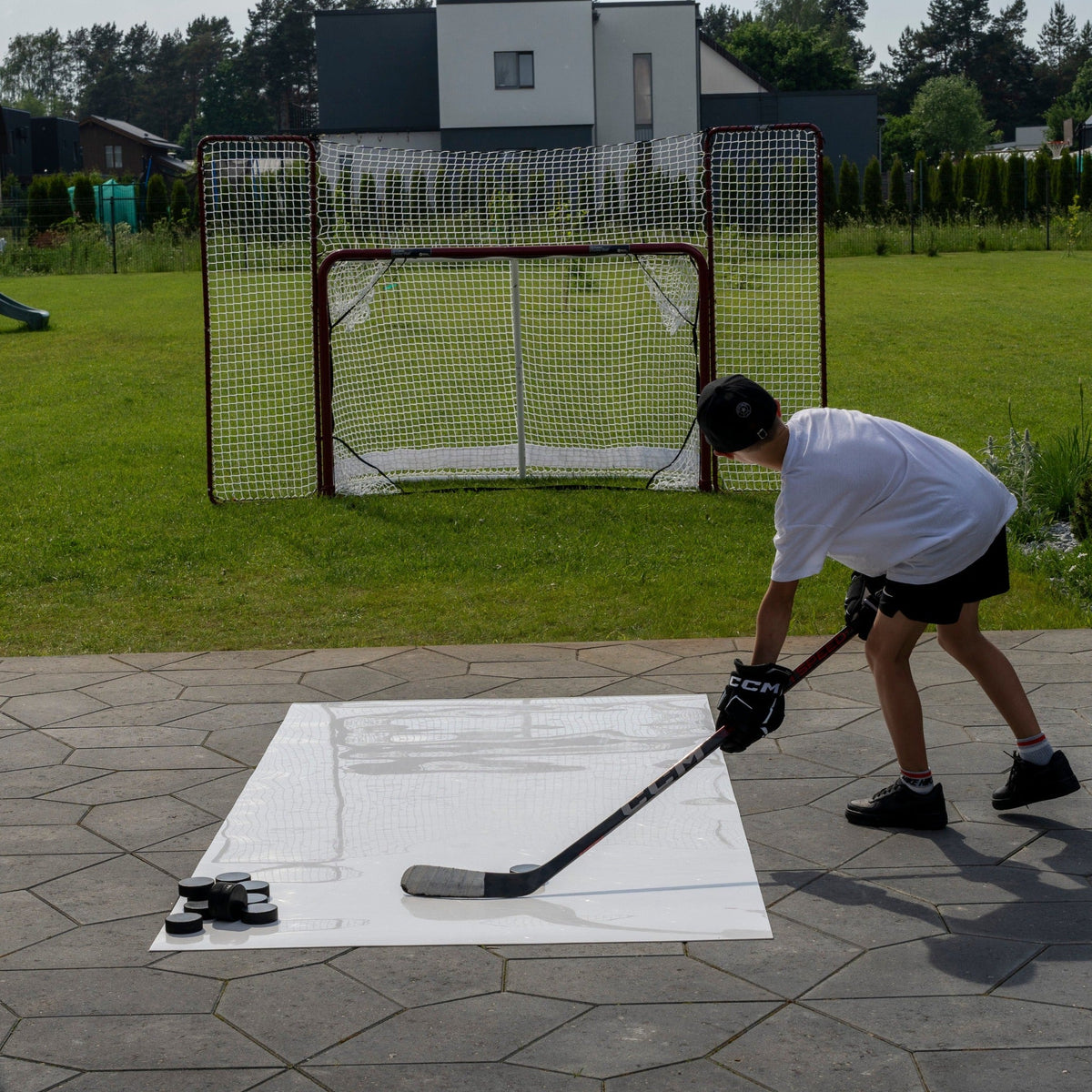Backyard home hockey training setup with a roll-up shooting pad, pucks, and a full-size goal with backstop