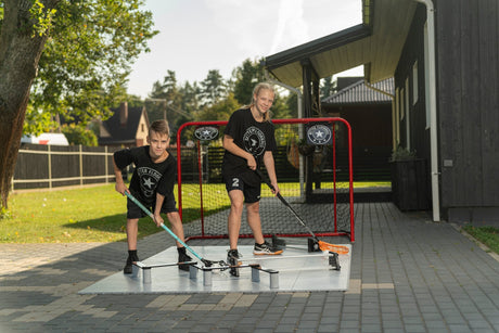 Two kids practising passing and shooting at the floorball goal