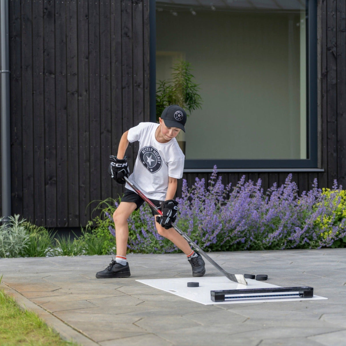 Young hockey player passing off the Extreme Hockey Rebounder on outdoor training tiles in natural light