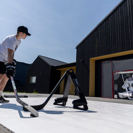 Hockey player stickhandling around a Pro Defender obstacle outdoors with a goal visible in the background